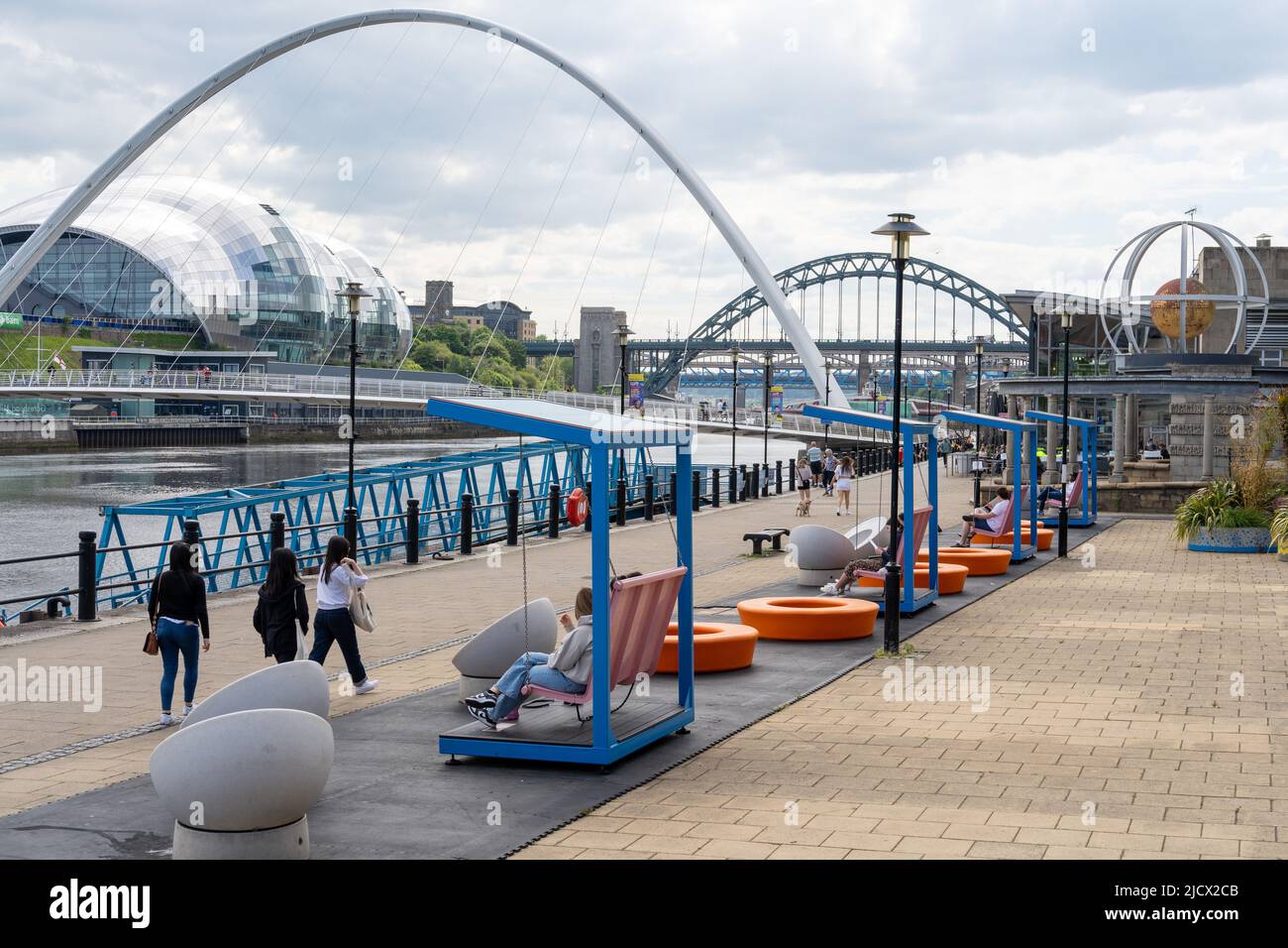 Blick auf den Quayside, Newcastle Upon Tyne, Großbritannien, mit Tyne-Brücken, einschließlich Gateshead Millennium Bridge und hellen modernen Sitzgelegenheiten. Stockfoto