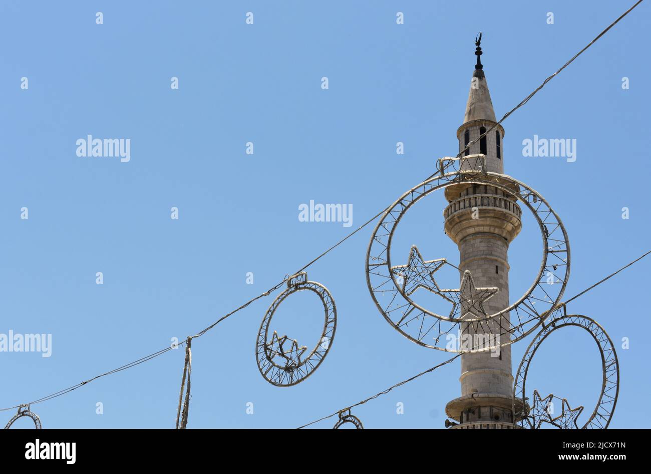 Ramadan-Dekorationen hängen in der Straße bei Eid vor einem Moschee-Minarett in Madaba in Jordanien Stockfoto