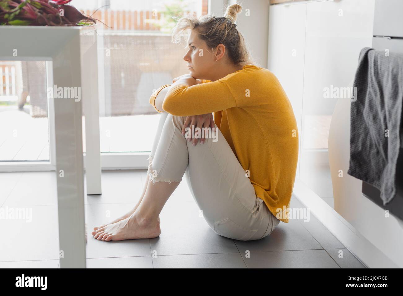 Einsame depressive und kranke Frau sitzt allein auf dem Küchenboden in Stress, Depression und Traurigkeit Gefühl elend in barfuß suchen verzweifelt Stockfoto