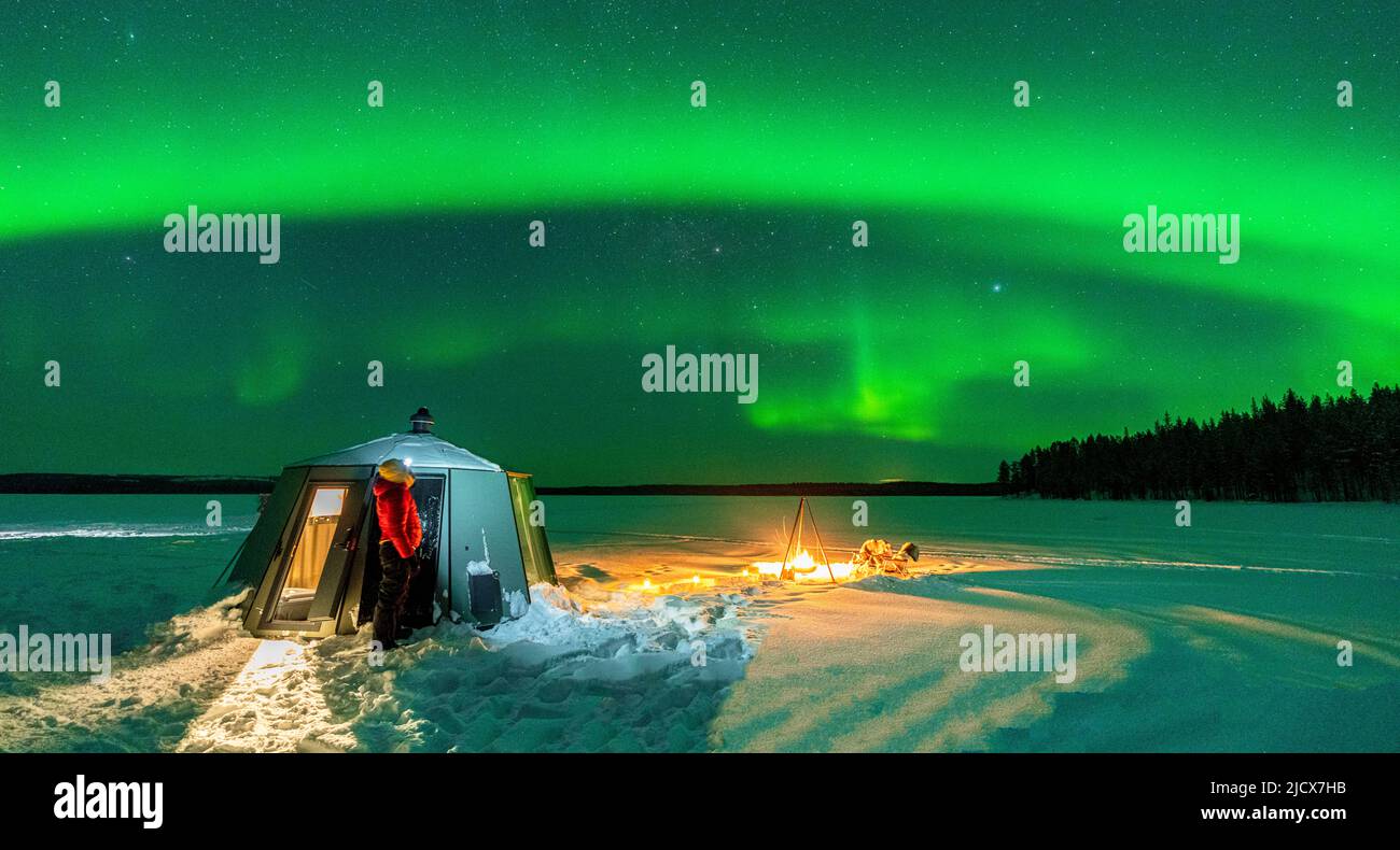 Wanderer beobachten die Aurora Borealis (Nordlichter) in der Nähe von Lagerfeuer und Iglu in der gefrorenen Landschaft, Jokkmokk, Lappland, Schweden, Skandinavien Stockfoto