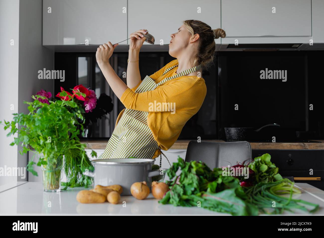 Cute Active 30 Jahre Frau Hausfrau hält Schöpfkelle wie Mikrofon singen tanzen in modernen gemütlichen Küche zu Hause Stockfoto