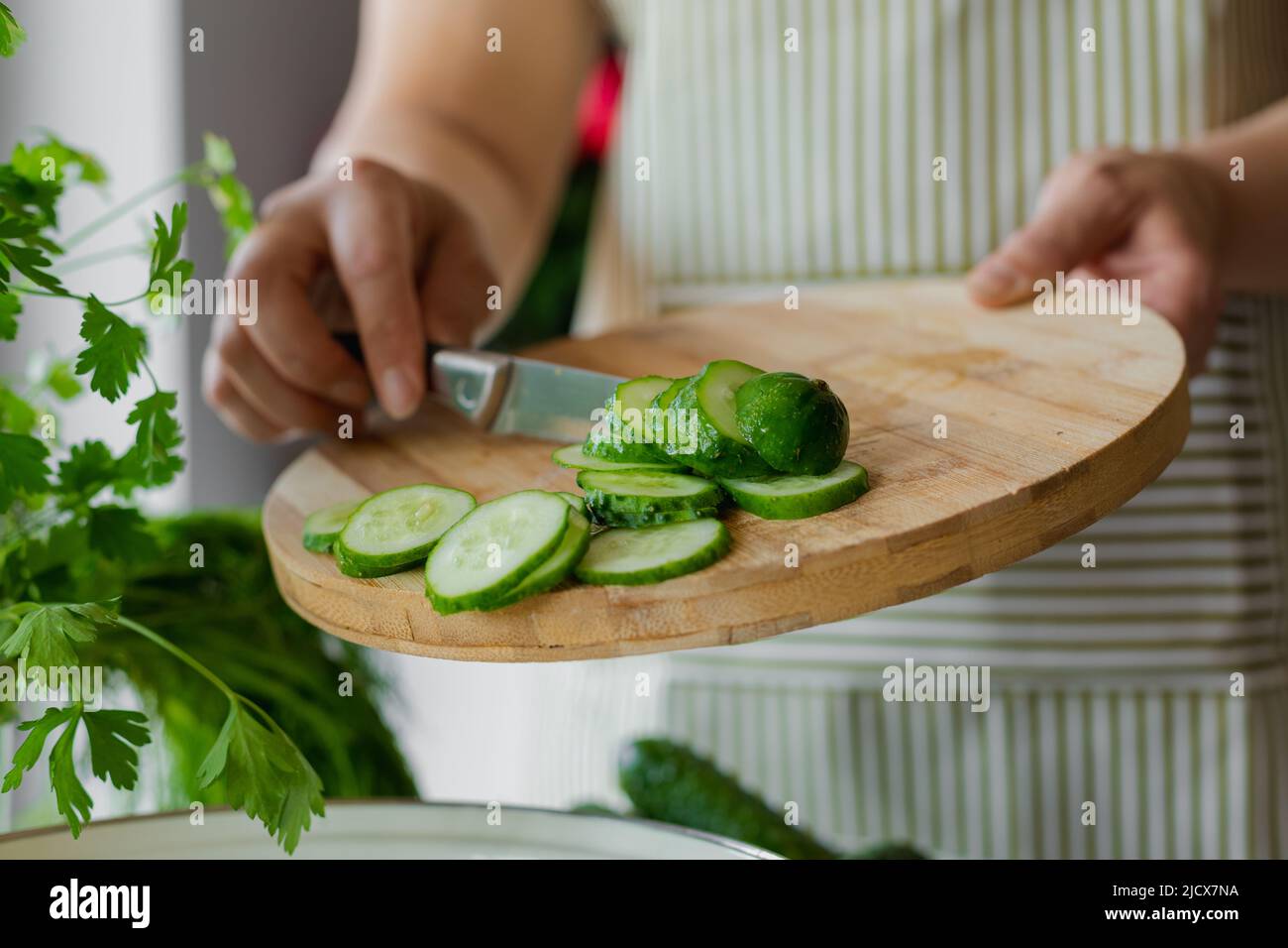 Frau schneidet Gurken für Salat auf Holzhintergrund, unkenntlich Person, Kochen zu Hause Stockfoto
