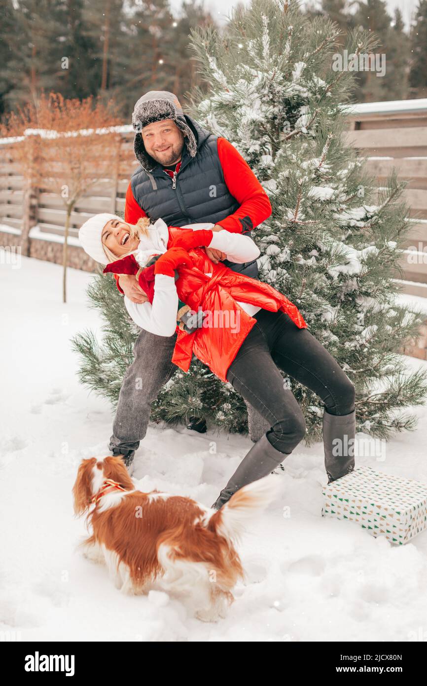 Mann und Frau spielen mit Schnee in schneebedeckten Vorder- oder Hinterhof, Menschen haben Spaß am Wintertag, Hund auf sie zu schauen Stockfoto