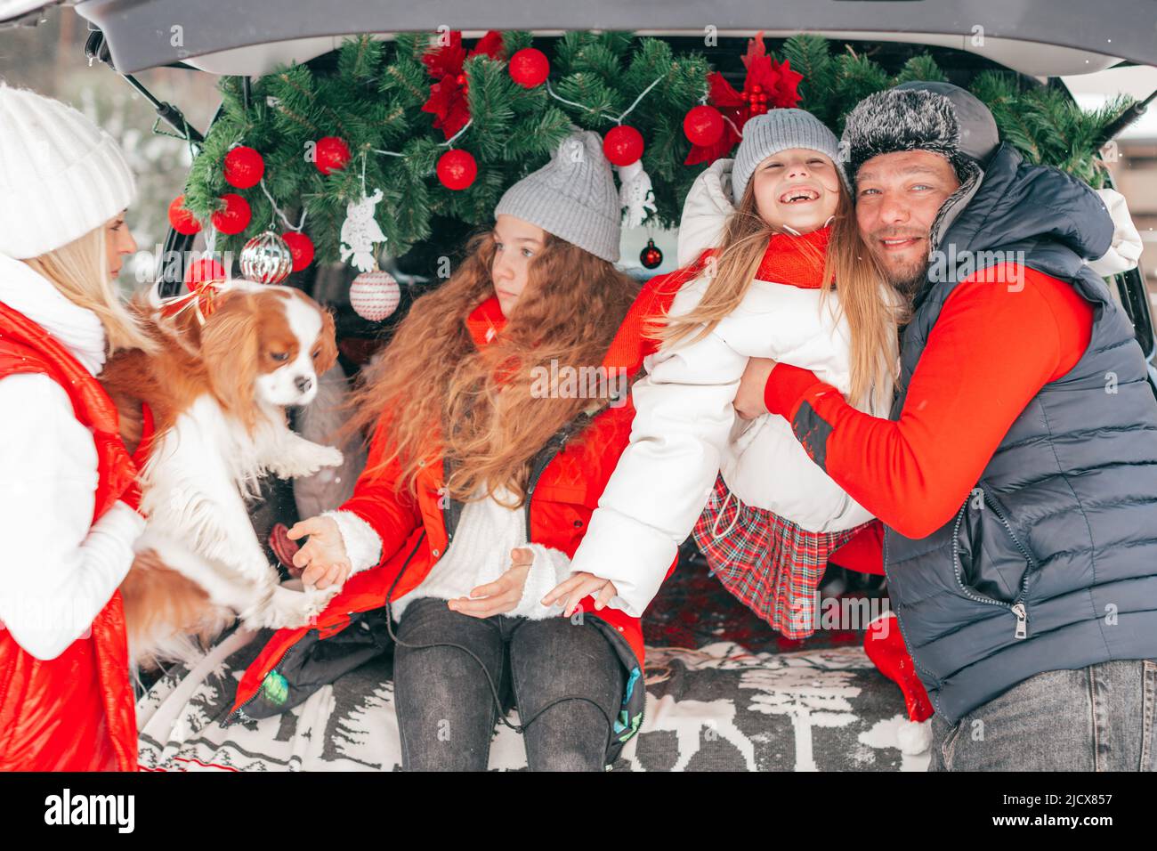 Entzückende Familie mit zwei Töchtern im Kofferraum der Familie. Glückliche gesunde Menschen, Kinder und Hund im Winter rote Mode Kleidung mit Weihnachtsfeier Stockfoto