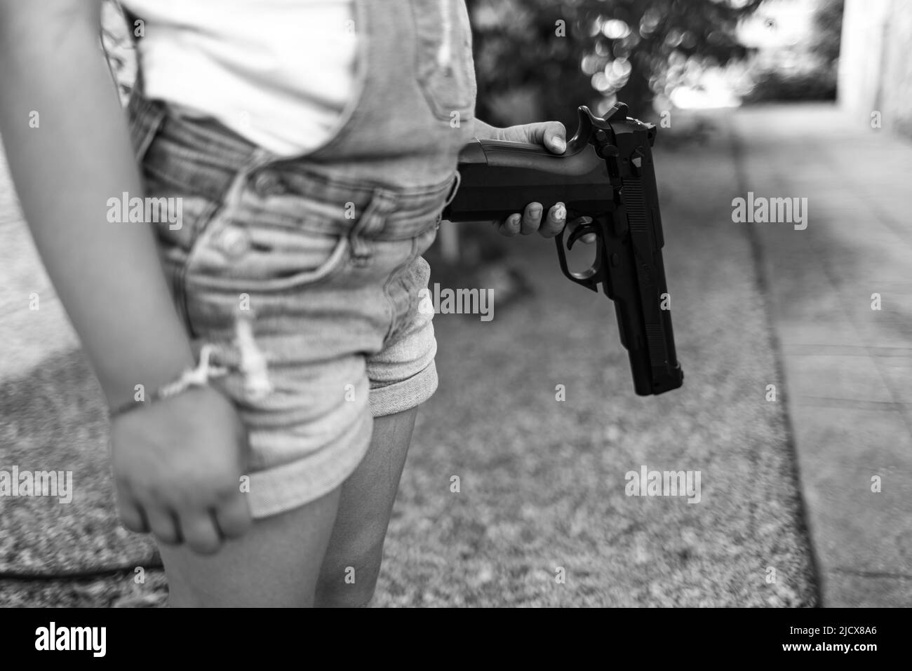 Schwarz-Weiß-Fotografie mit einem kleinen Mädchen, das eine Pistazie in der Hand hält und auf den Boden zeigt. Konzept der Gewalt, Waffen, Waffen, Kindheit, USA, Schießen Stockfoto