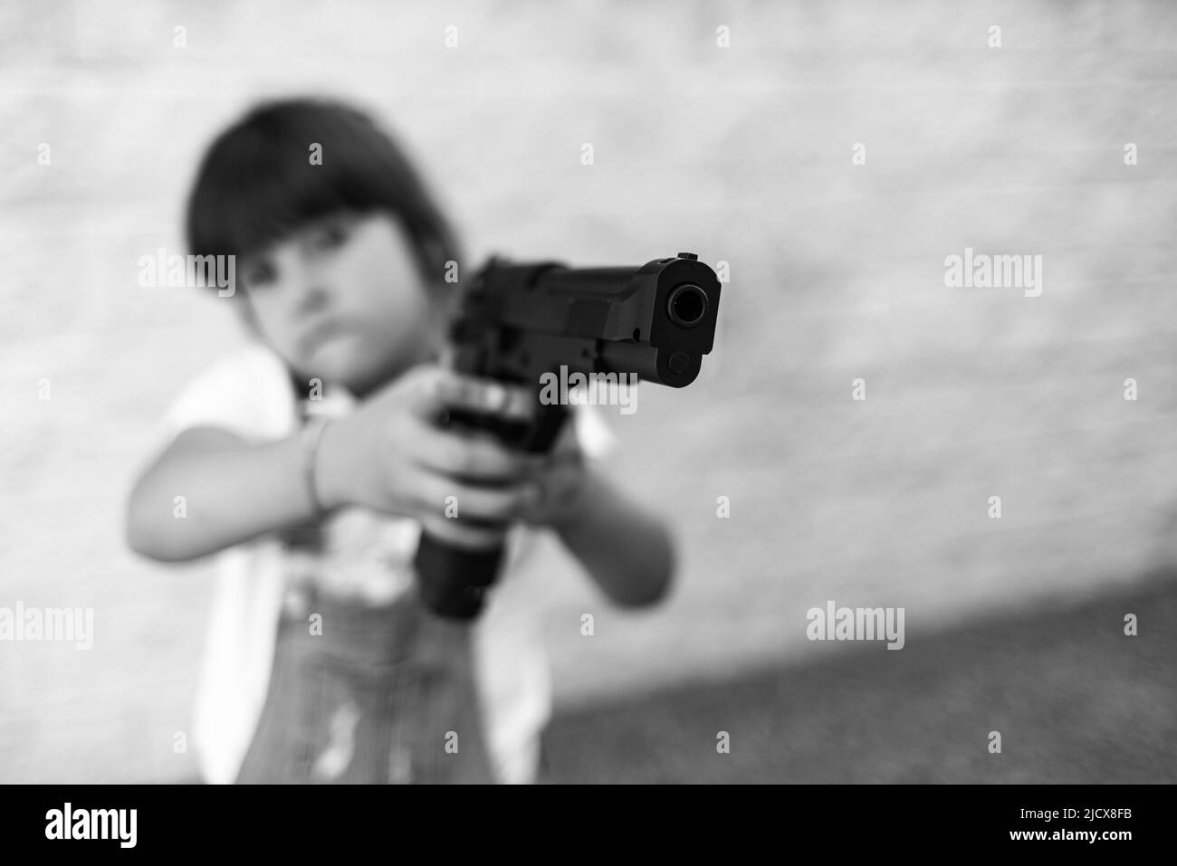 Schwarzweiß-Fotografie mit einem kleinen Mädchen, das auf eine Waffe zeigt. Konzept der Gewalt, Waffen, Waffen, Kindheit, USA, Schießen, Mord und Tod. Stockfoto