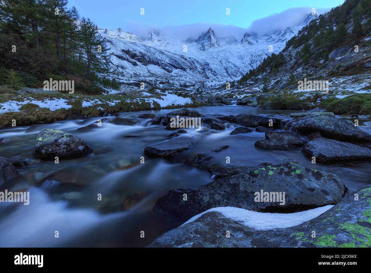 Gebirgsbach bei Dämmerung vor verschneiten Bergen, Valmasino, Valtellina, Lombardei, Italien, Europa Stockfoto