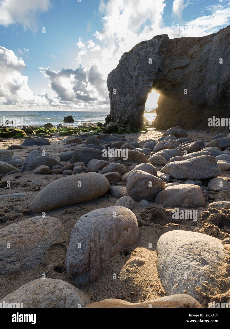 Steine an einem Strand mit dem Licht, das durch den natürlichen Bogen von Port Blanc, Quiberon, Bretagne, Frankreich, Europa geht Stockfoto