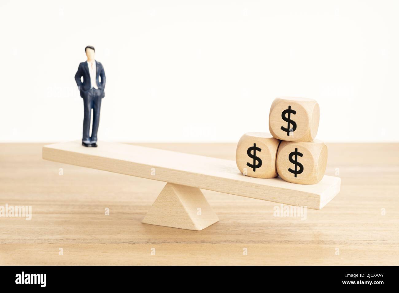 Leben und Arbeit oder Geld Balance Konzept. Businessman-Figur und Dollarsymbol auf Holzblöcken auf hölzerner Wippe Stockfoto