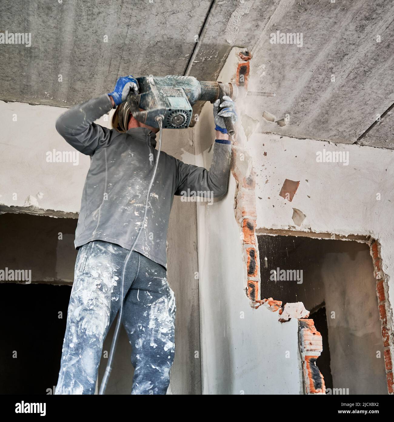 Dismantler stürzt im Aufprallmodus durch Perforator in die Zwischenwand. Überholung mit Abriss der angrenzenden Wände, um den Wohnraum zu vergrößern. Stockfoto