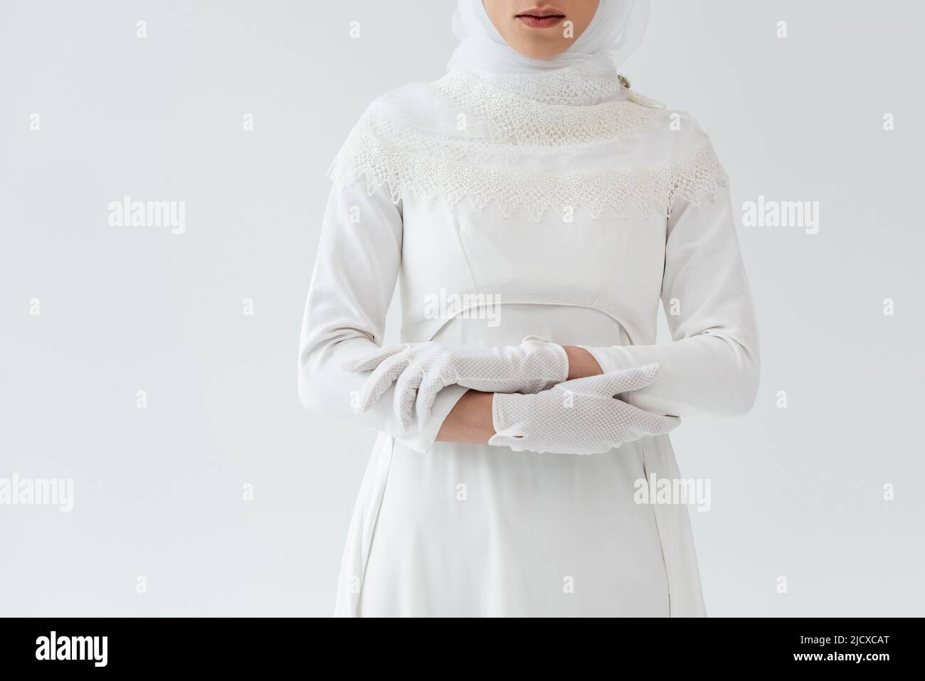 Verkürzte Ansicht der jungen muslimischen Braut in Handschuhen und weißem Kleid isoliert auf grau Stockfoto