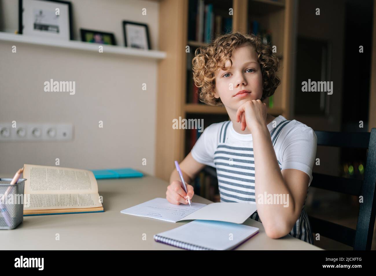 Portrait of adorable lockig kleine Schülerin zu Hause studieren, Hausaufgaben machen, Stift halten, Notizen schreiben, Blick auf die Kamera. Stockfoto
