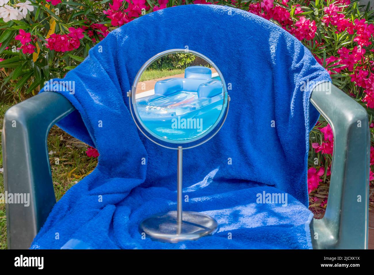 Ein Gartenstuhl mit einem blauen Handtuch und einem Spiegel, der einen Swimmingpool mit Luftmatratze reflektiert Stockfoto