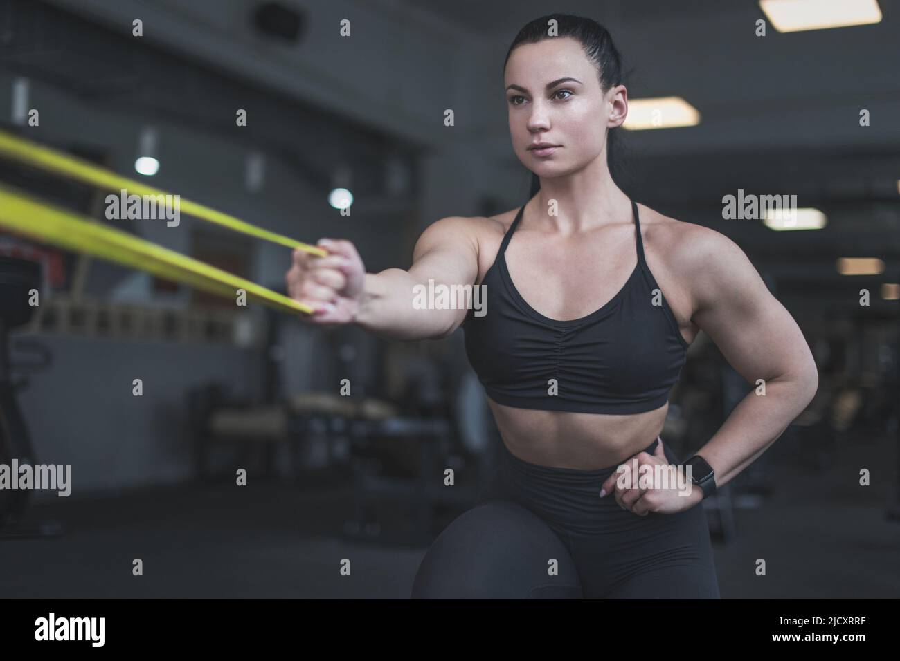 Muskulöse junge Frau beim Aufwärmen mit gelbem Gummiband im Fitnessstudio Stockfoto