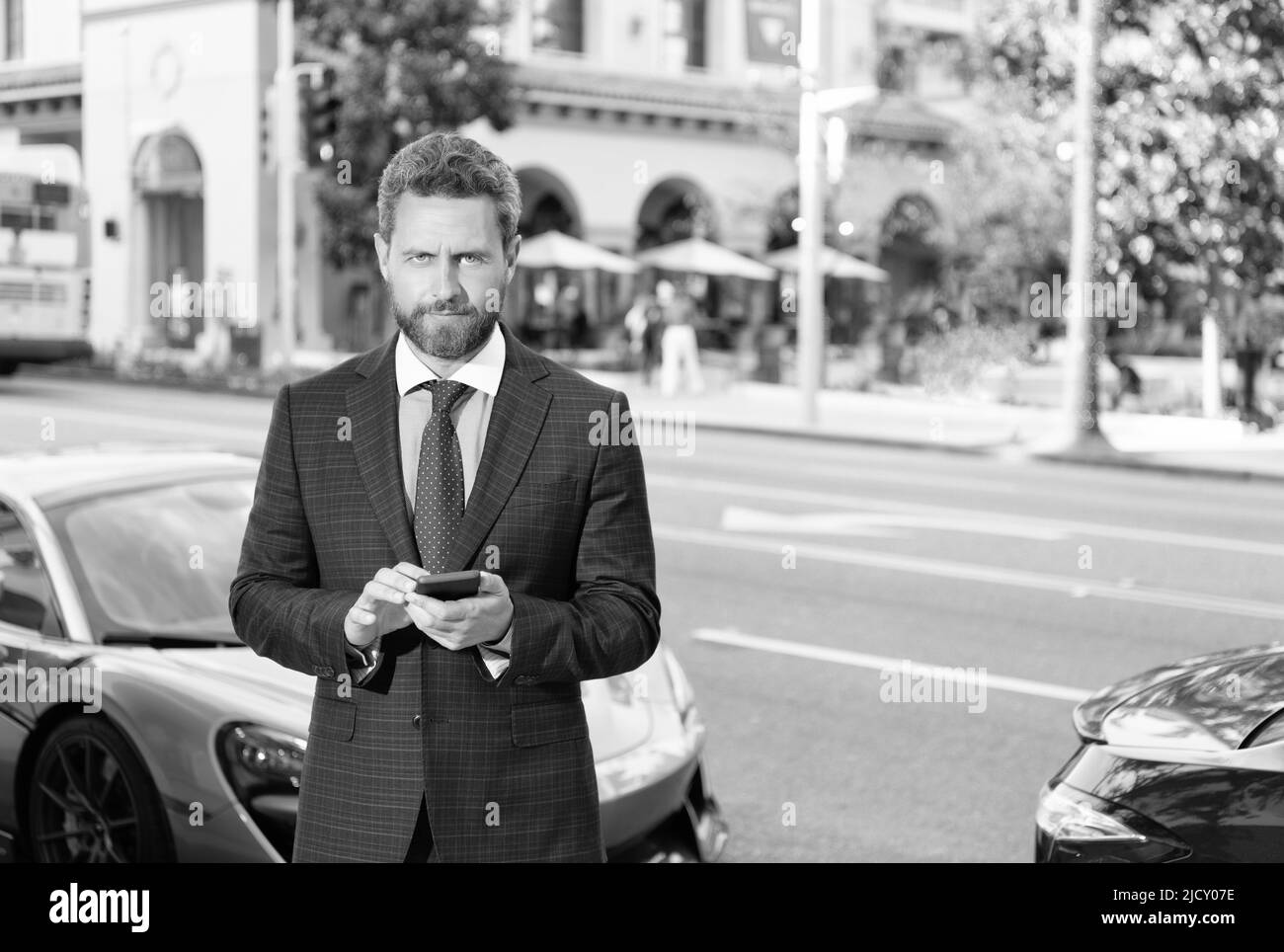 Erfolgreicher Mann im Anzug steht für Auto SMS auf Smartphone, kopieren Raum, mieten online. Stockfoto