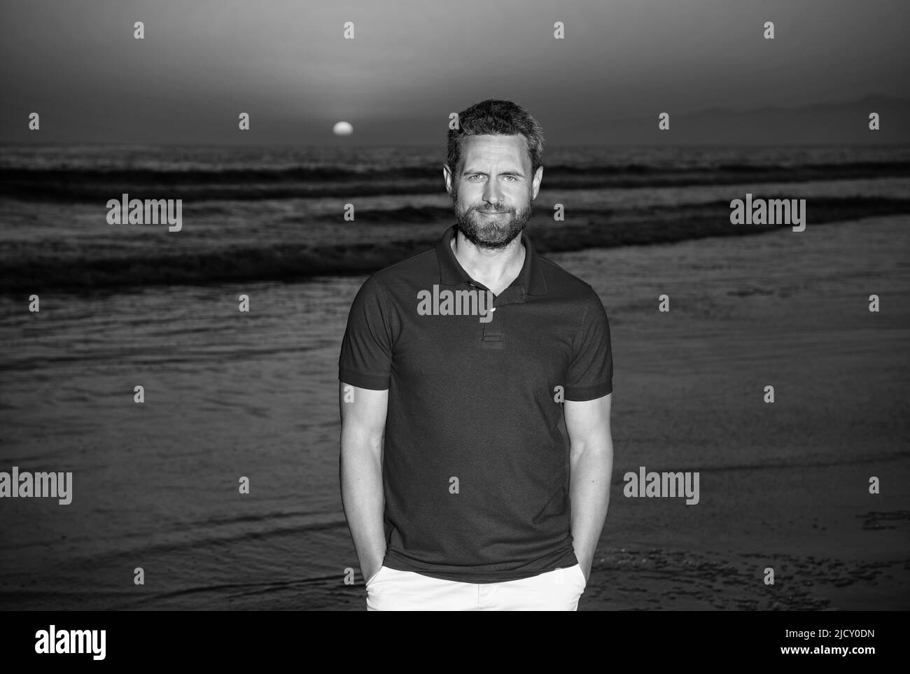 Sommerurlaub. Positive Emotionen. Lächelnder Mann mit Bart bei Sonnenuntergang über Meer. Stockfoto