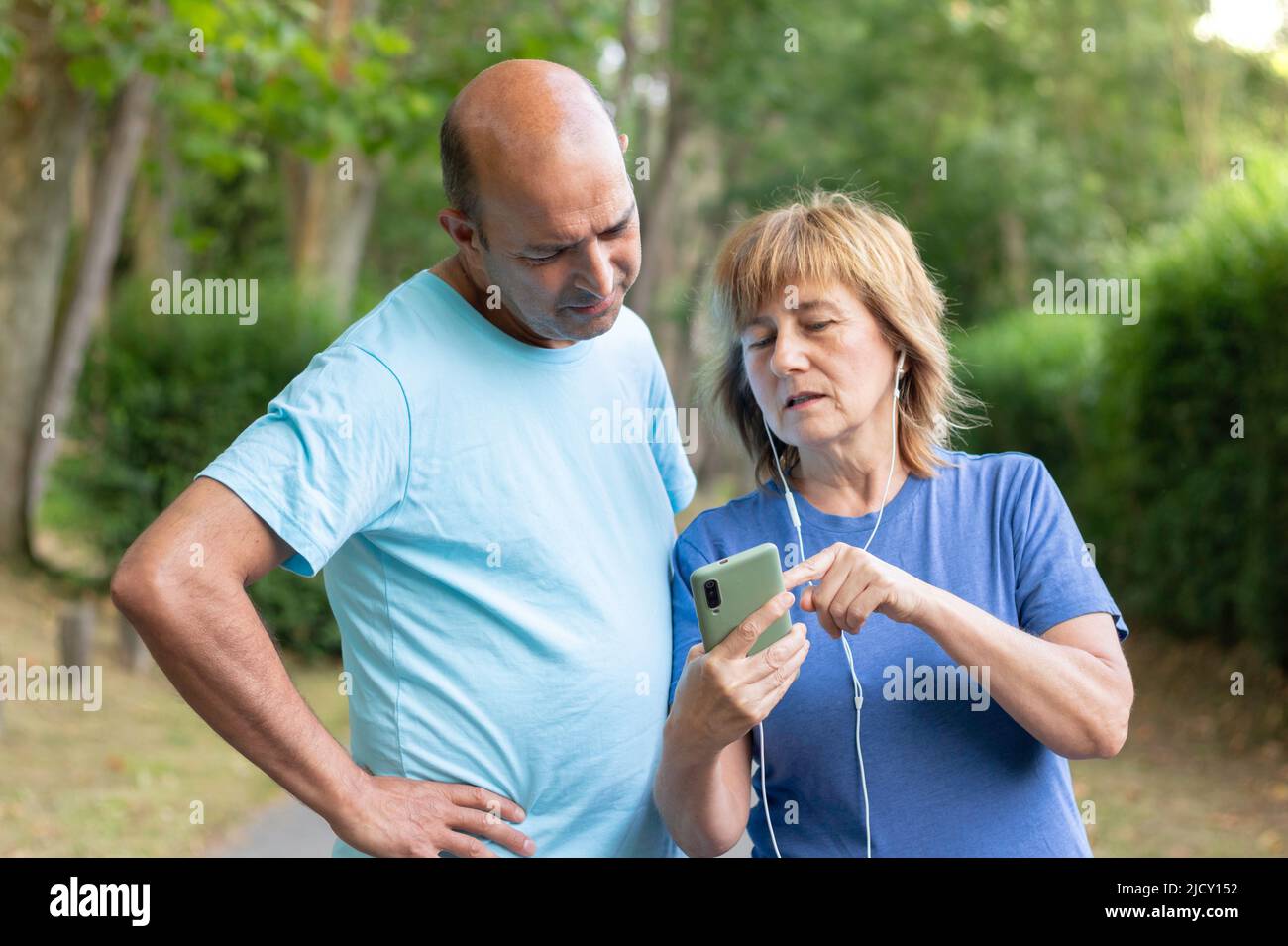 Reifes erwachsenes Paar, das durch den Park schlendert, während die Frau dem Mann ein Foto auf ihrem Mobiltelefon zeigt Stockfoto