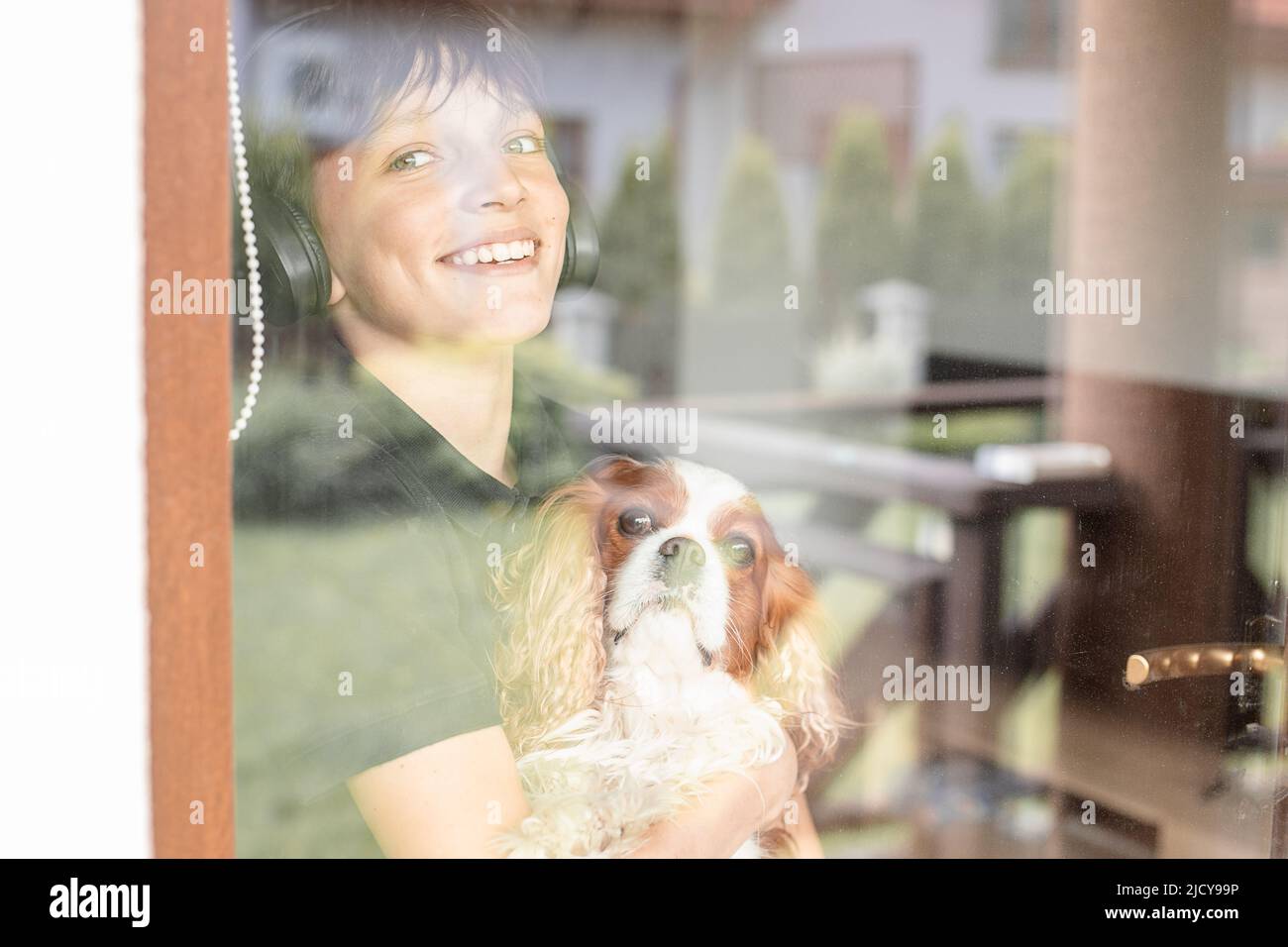 Porträt eines lächelnden fröhlichen Teenagers Junge mit Hund Cavalier King Charles spaniel, durch das Fenster schauen, posieren. Stockfoto
