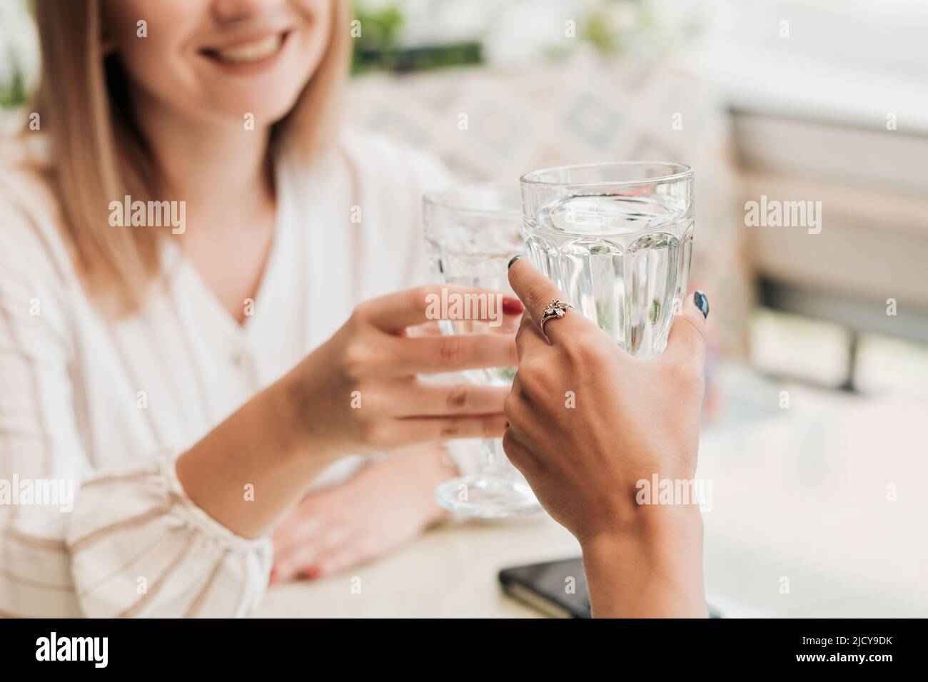 Nahaufnahme von zwei nicht erkennbaren Frauen, die an Wassergläsern klopfen, Frauen, die im Restaurant eine Mittagsbesprechung haben Stockfoto