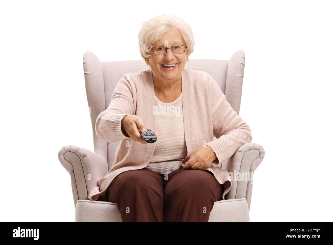 Ältere Frau, die in einem Sessel sitzt und eine fernbedienung auf weißem Hintergrund hält Stockfoto