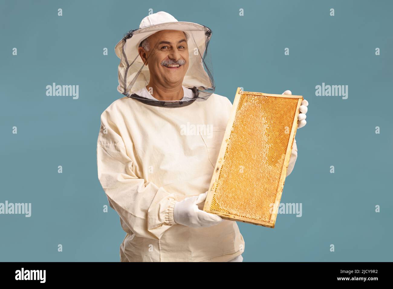 Reifer männlicher Bienenhalter in einer Uniform, der einen Honigbienenrahmen auf blauem Hintergrund isoliert hält Stockfoto
