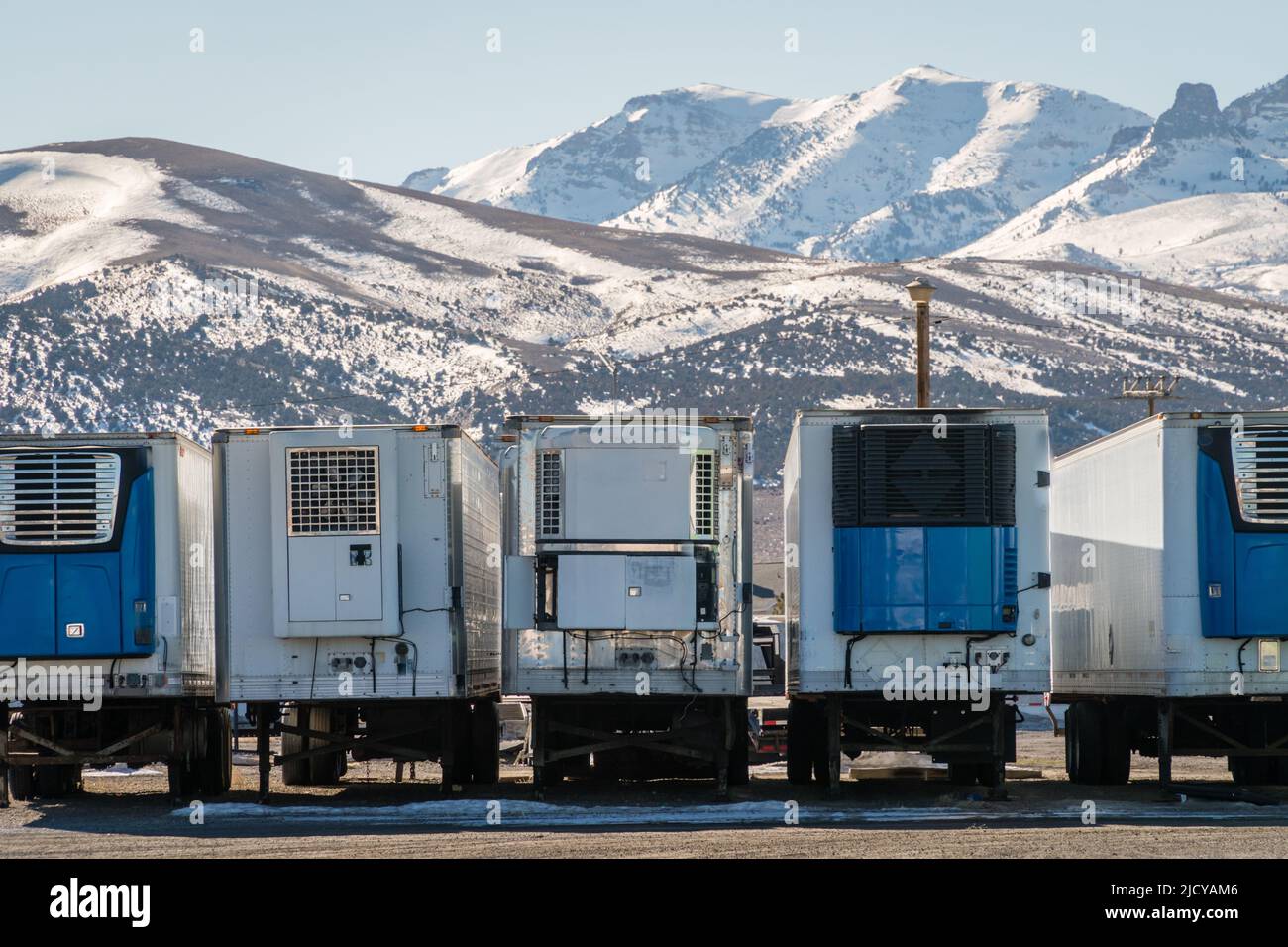 Reihe von LKW-Anhängern mit verschneiten Bergen im Hintergrund Stockfoto
