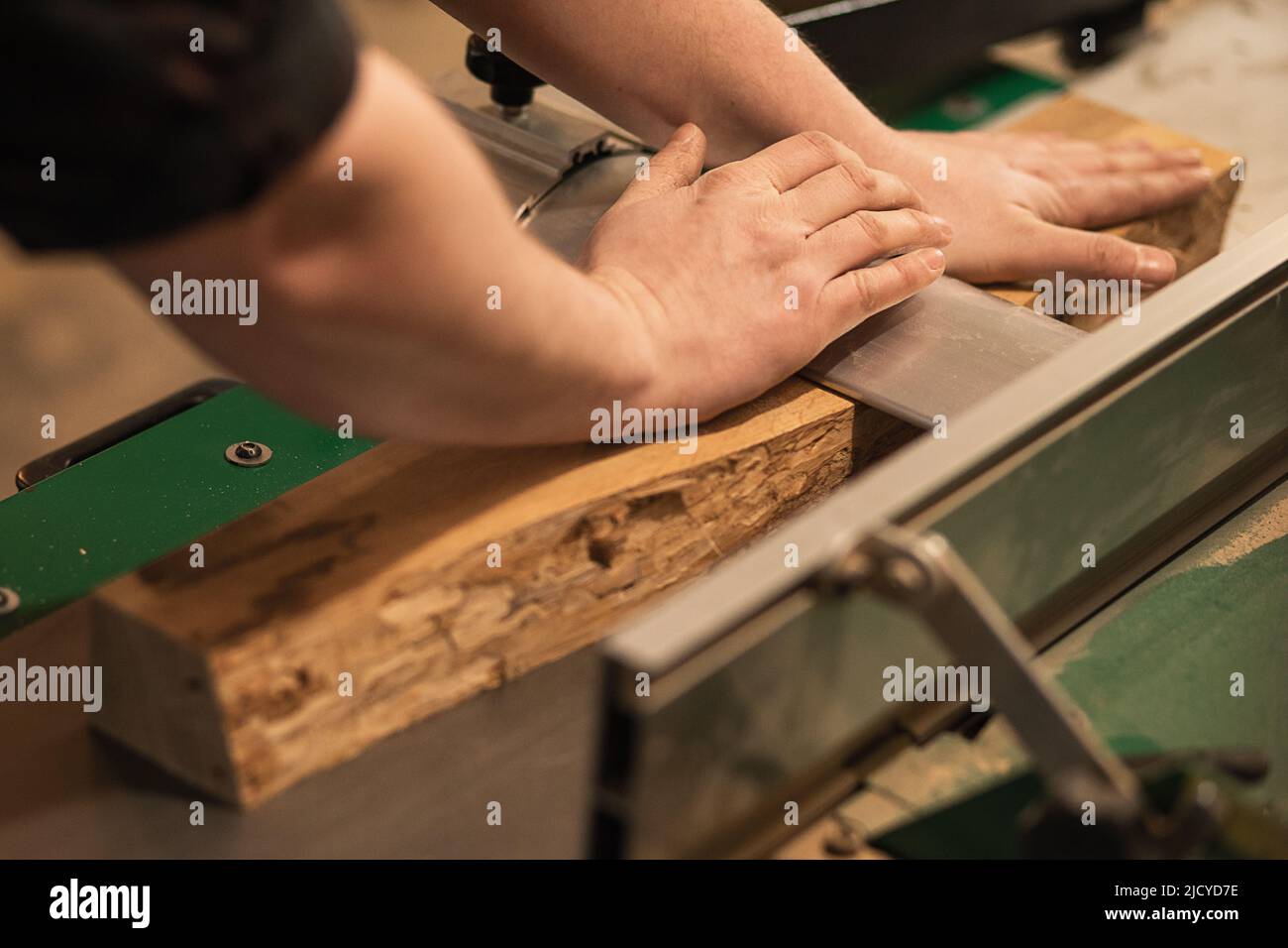 Nahaufnahme des Zimmermanns, Tischlerarbeiters Hände drücken, drücken nach unten, setzen Holzbrett auf Schneidemaschine in der Werkstatt Stockfoto