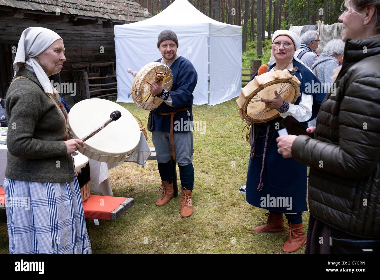 Menschen in traditionellen lettischen Kostümen spielen Tierhauttrommeln im Ethnographischen Freilichtmuseum von Lettland, Riga, Lettland Stockfoto