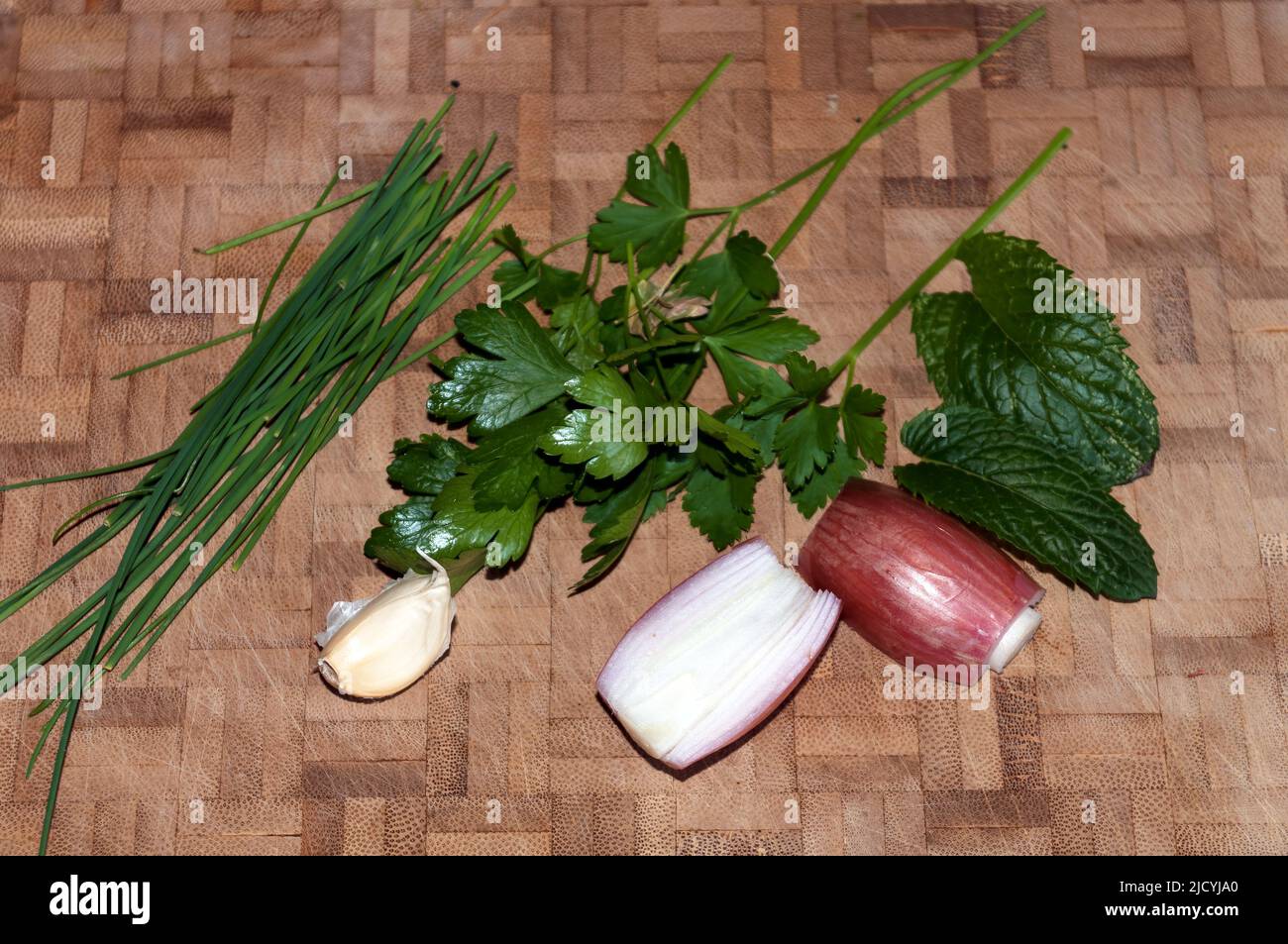 Knoblauch, Zwiebeln, Schnittlauch, Minze und Petersilie auf einem Holzbrett Stockfoto