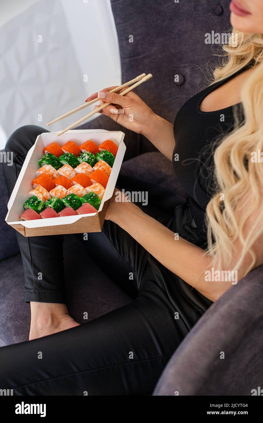Essen von Sushi mit Essstäbchen aus der Nähe, Essen zum Mitnehmen und Lieferservice, Lachs-Sushi-Brötchen, leckeres Essen, Sushi-Lieferung. Stockfoto