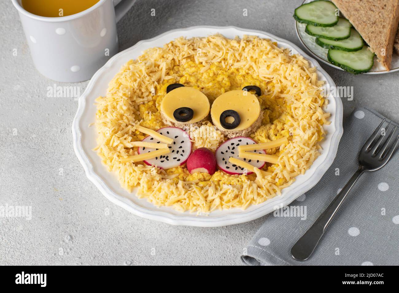 Tolles Essen für Kinder zum Frühstück - süßer Löwenkopf aus Rührei, Käse, Radieschen und schwarzen Oliven auf weißem Teller Stockfoto