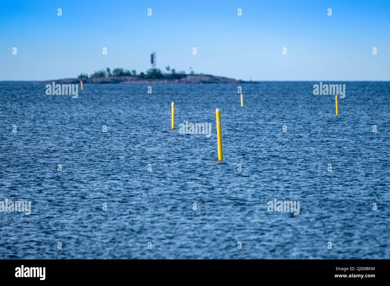 Helsinki / Finnland - 15. JUNI 2022: Eine Reihe von gelben Navigationsbojen, die auf dem Wasser schweben. Eine kleine Insel im Hintergrund. Stockfoto