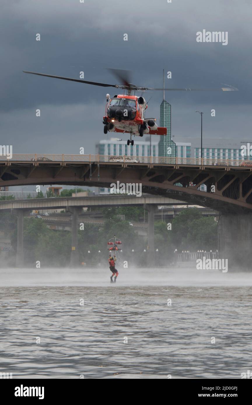 Ein Survival-Techniker der Küstenwache hält sich an den Korb, der von einer Hubschraubermannschaft des Typs MH-60 Jayhawk auf dem Willamette River in Portland, Oregon, am 11. Juni 2022 aus dem Wasser gezogen wurde. Die AST leitete die Bereitstellung des Warenkorbs für die Demonstration. (USA Foto der Küstenwache von Petty Officer, Klasse 3., Diolanda Caballero) Stockfoto