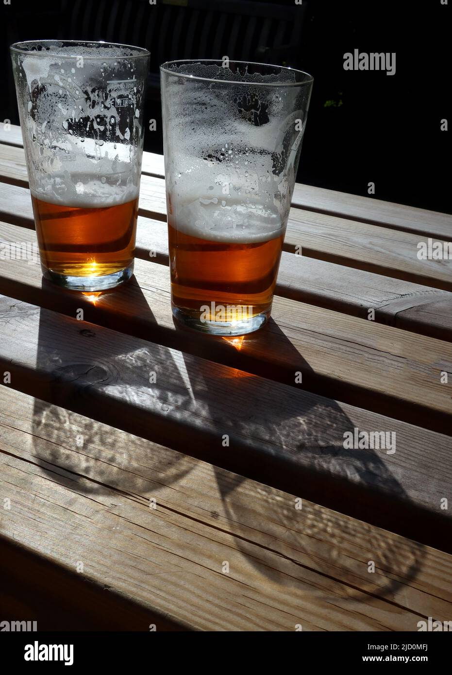 Glas Half Full - 2 Pint Topfgläser mit echtem Ale, die einen Abendschatten über einem Biergartentisch werfen, Cheshire, England, Großbritannien Stockfoto