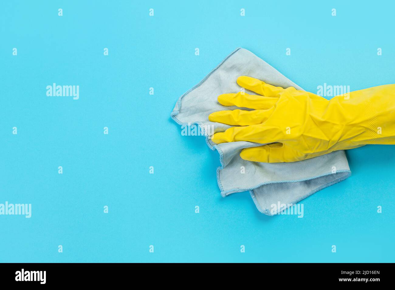Arbeiter Hand in einem gelben Gummi-Schutzhandschuh mit einem mikrofaserblauen Tuch, das eine blaue Wand vom Staub abwischt. Ein Zimmermädchen oder eine Hausfrau kümmert sich um das Haus. Stockfoto