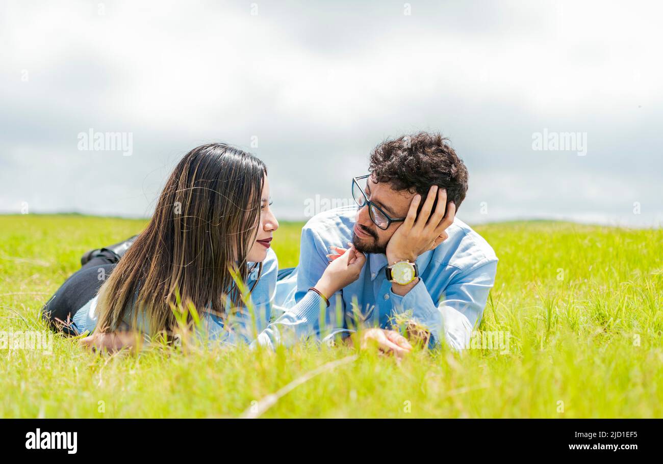 Zwei verliebte Menschen liegen auf dem Gras und schauen sich an, Ein Paar liegt auf dem Gras und schaut sich an, Junges Paar verliebt liegt auf dem Stockfoto