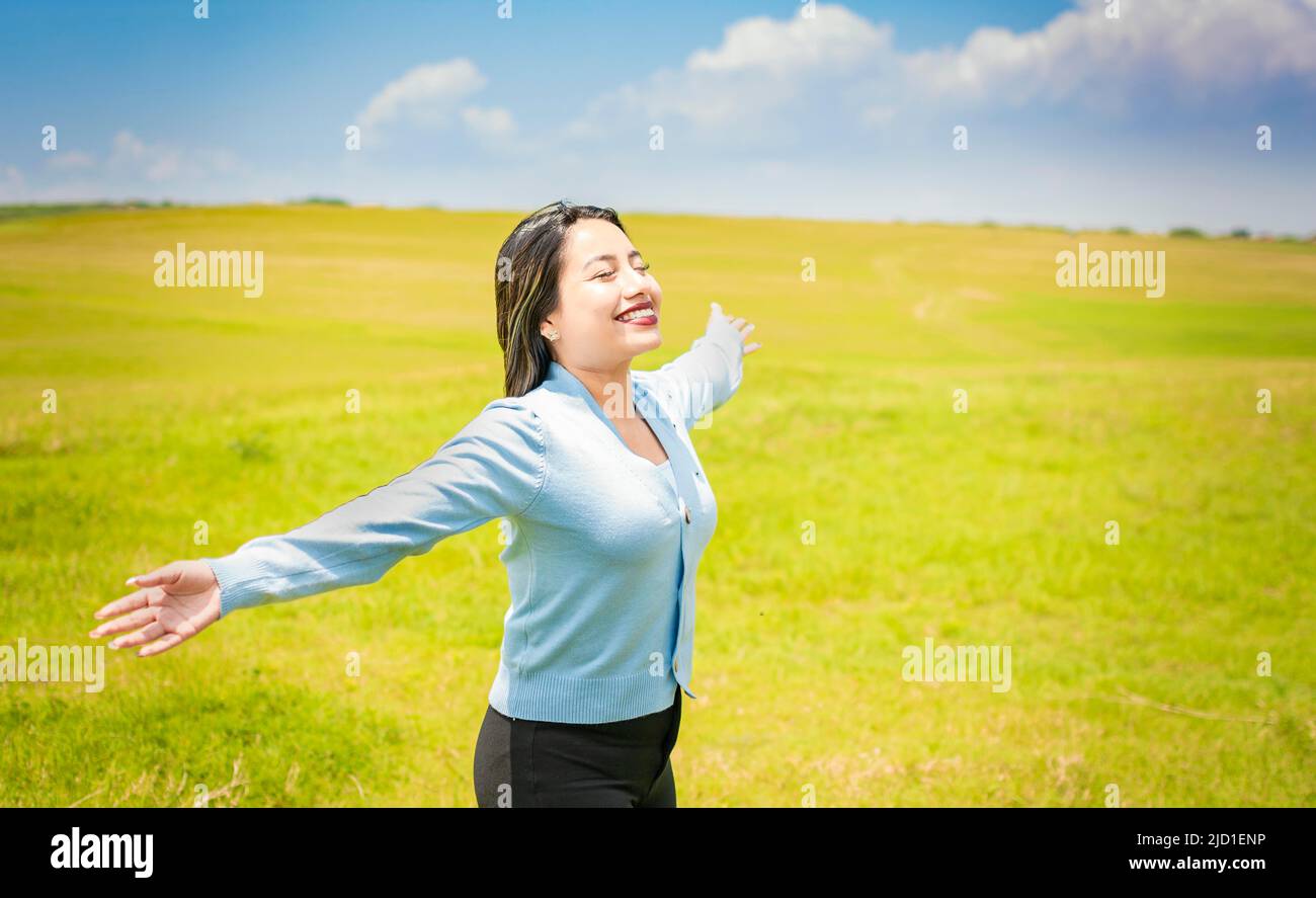 Junge Frau lächelt und breitet ihre Hände auf dem grünen Feld aus, Konzept einer Frau, die frische Luft auf dem Feld atmet, einer glücklichen Frau, die frische Luft einatmet Stockfoto