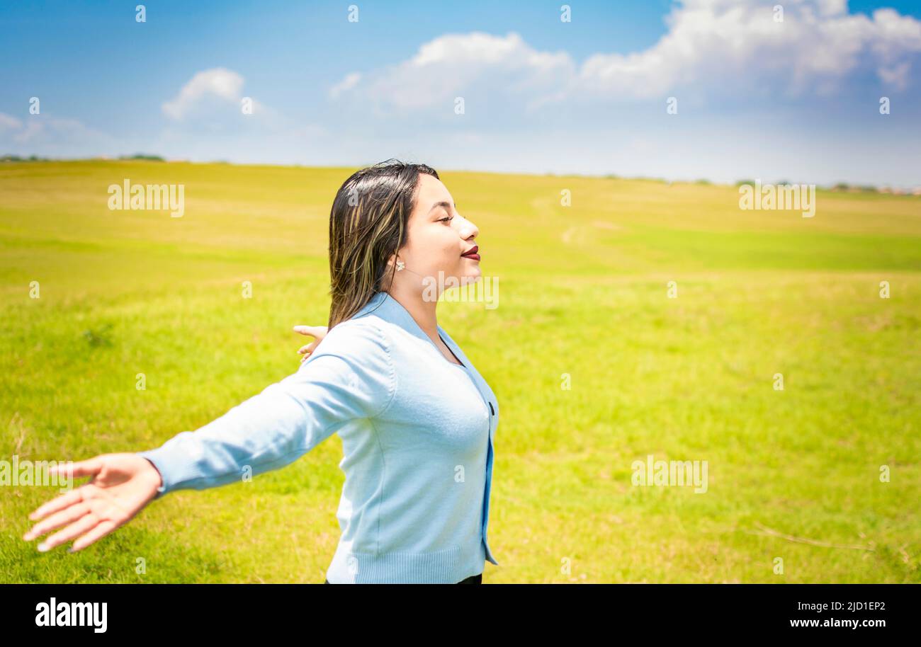 Glückliche Frau, die frische Luft auf dem Feld atmet und Arme ausbreitet, junge Frau lächelt und ihre Hände im grünen Feld ausbreitet, Konzept der Frau Stockfoto