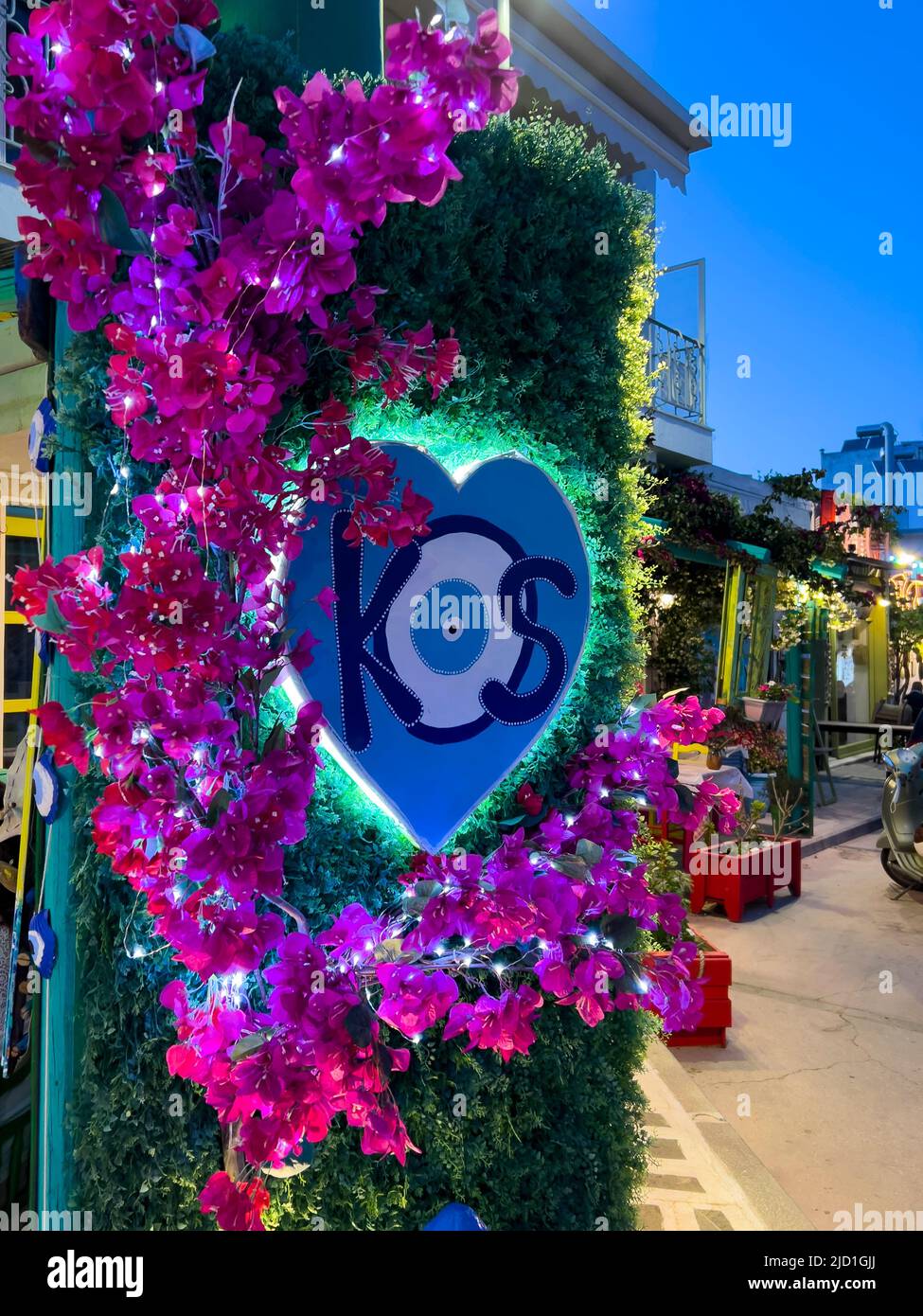 Kos-Griechenland, 05.31.2022: Geschäfte im Stadtzentrum von Kos Island. Traditionelles böses Auge-Design mit KOS-Text, umgeben von rosa Bougainvillea-Blumen Stockfoto