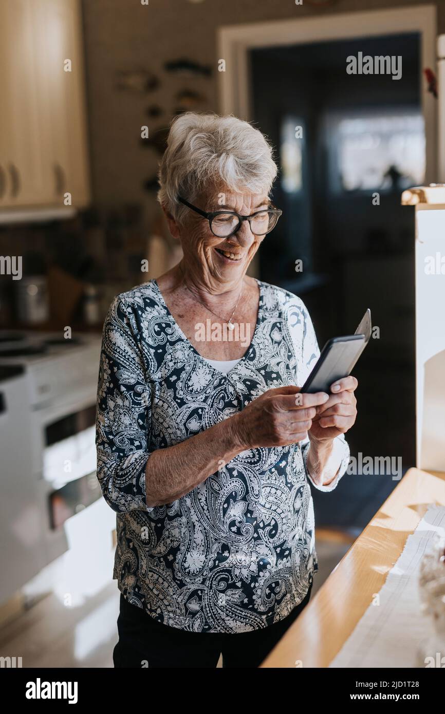 Ältere Frau benutzt Handy in der Küche Stockfoto