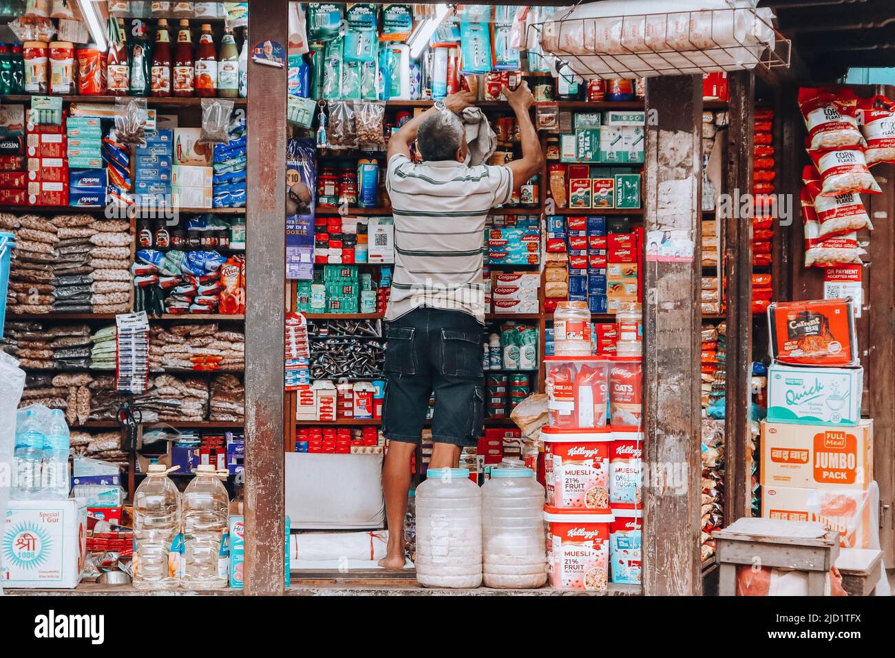 Alter Mann, der die Waren in seinem kleinen Laden in Bhaktapur putzte. Stockfoto
