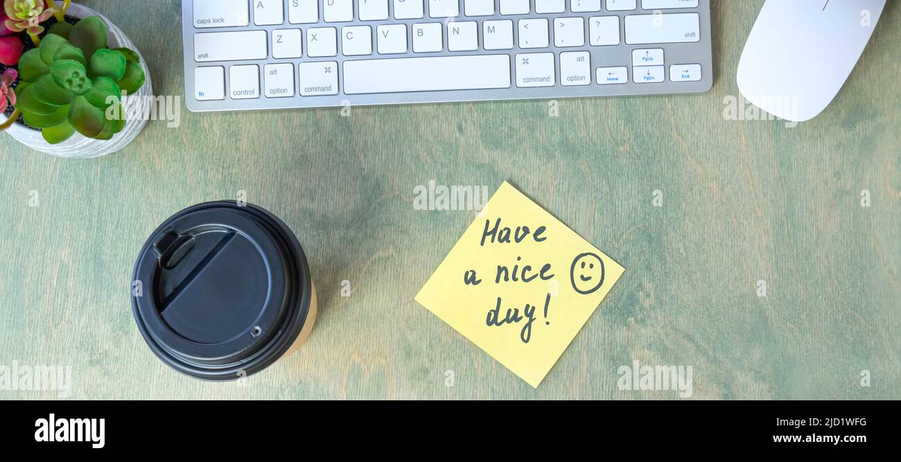 Banner mit Notiz mit Worten HABEN Sie Einen SCHÖNEN TAG mit Lächeln und Kaffee in Papperbecher, Tastatur, Kaktus und Mause auf einem Holztisch. Konzept des guten Start t Stockfoto