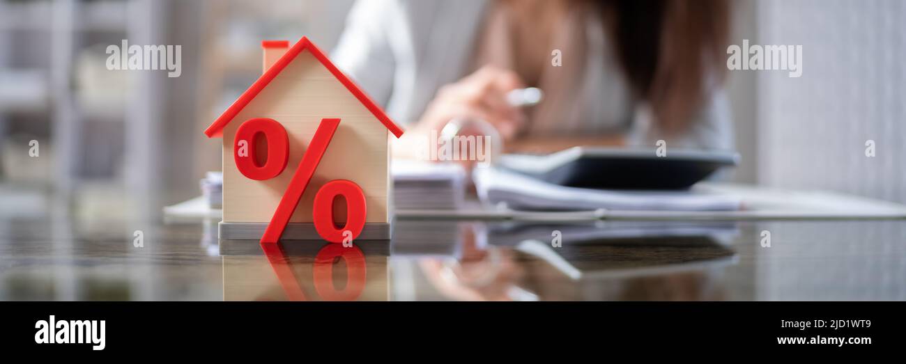 Nahaufnahme eines Hauses Modell mit Prozentzeichen und roten Dach auf hölzernen Schreibtisch Stockfoto