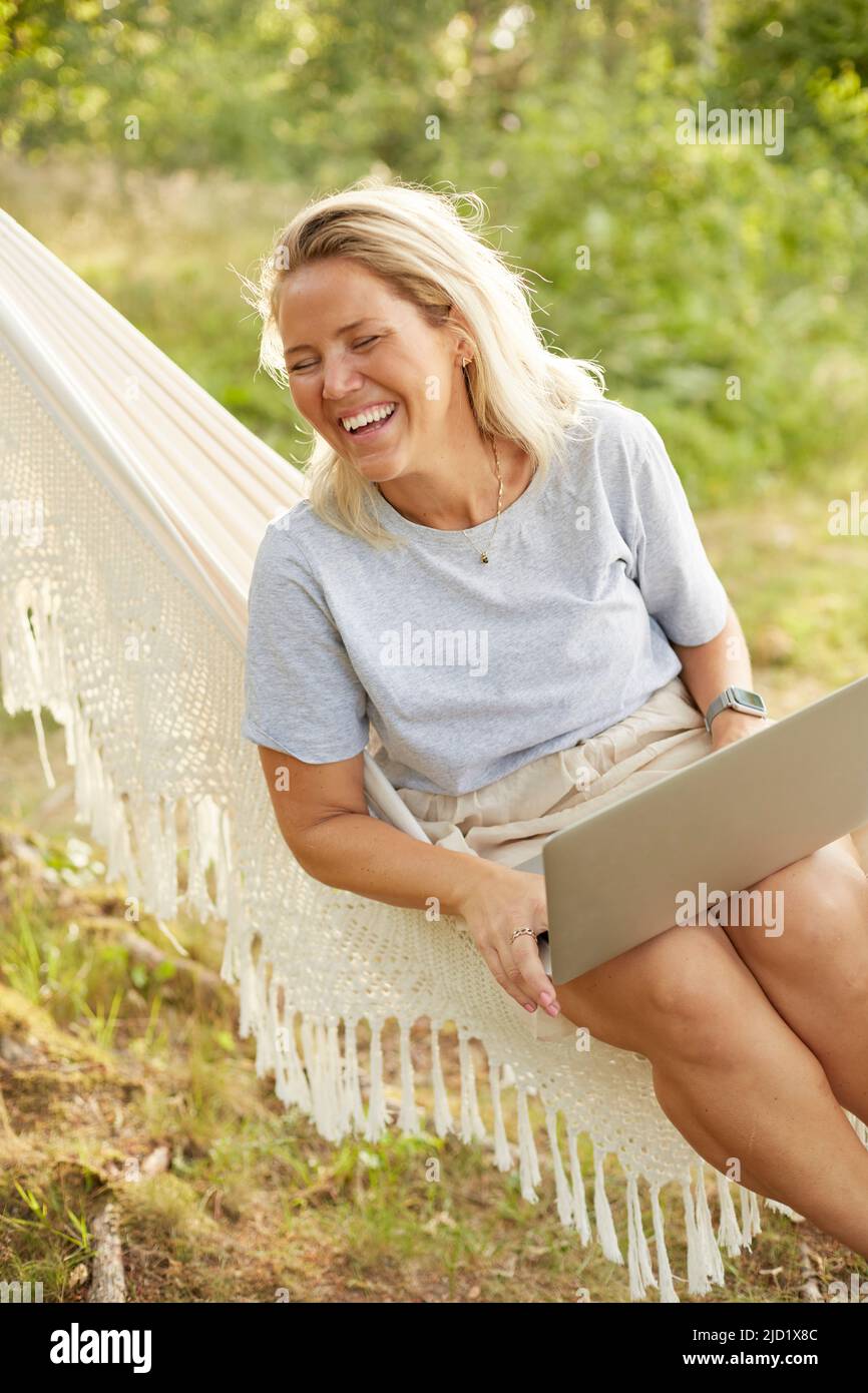 Frau mit Laptop in Hängematte Stockfoto