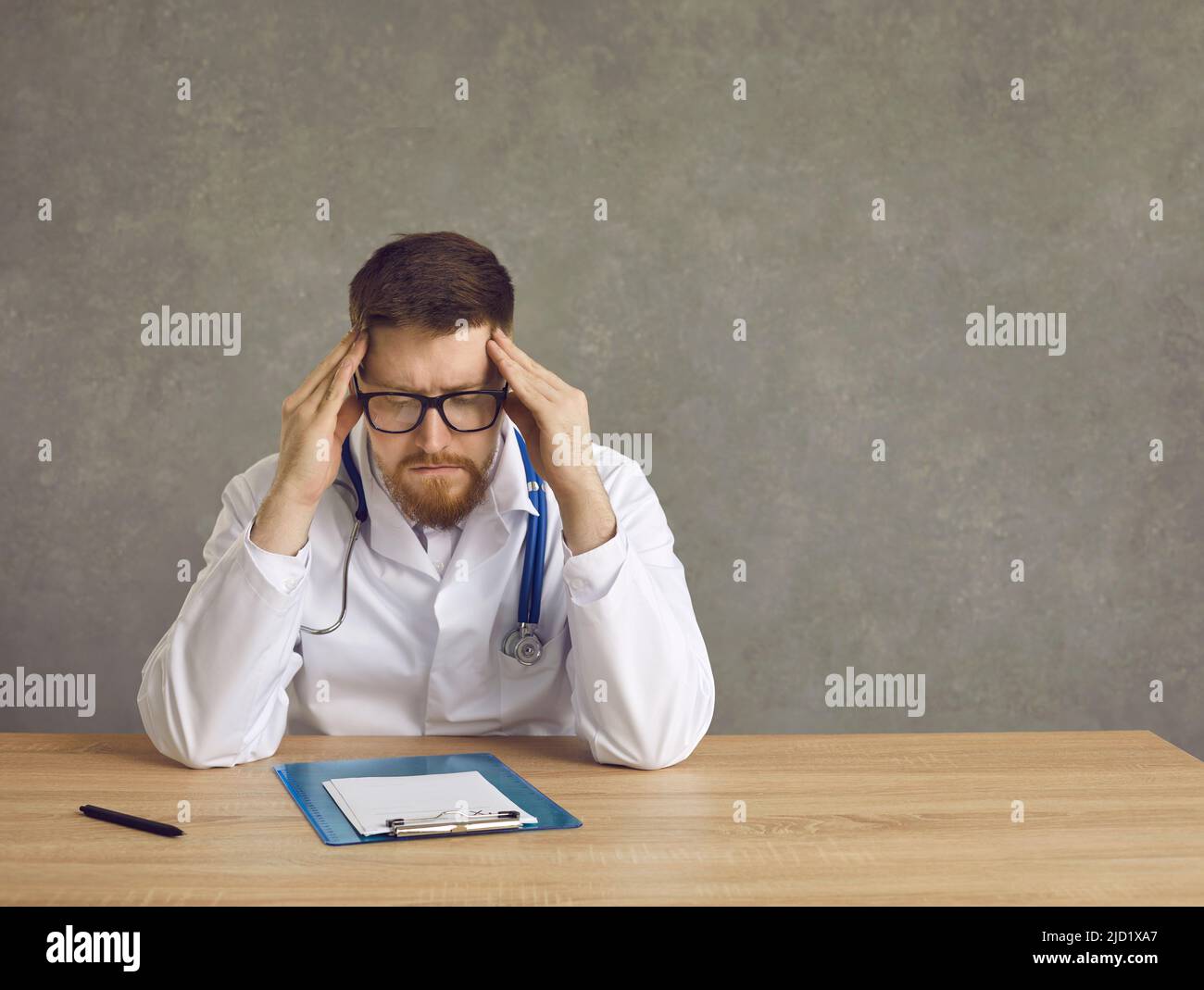 Erschöpfter männlicher Arzt, der unter Kopfschmerzen leidet, gestresstes Studiofoto Stockfoto