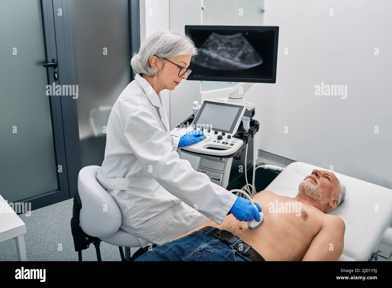 Ultraschallspezialist, der mit einem Ultraschallgerät im Krankenhaus eine Ultraschalluntersuchung der Bauchhöhle bei reifen männlichen Patienten macht Stockfoto