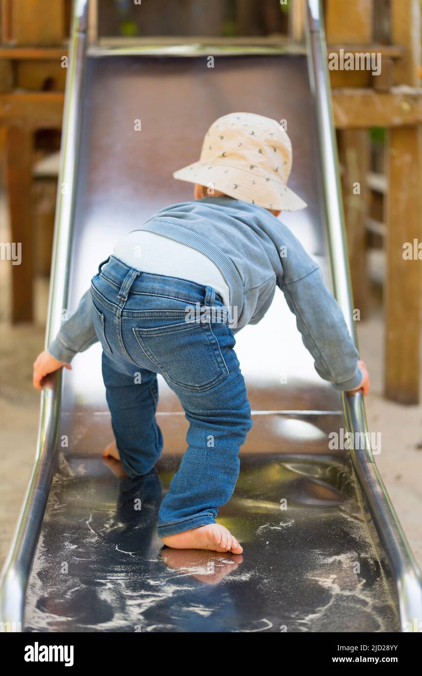 Rückansicht des Kleinkindes, das die Rutsche hochklettert, ein einjähriger Junge, der die Rutsche auf dem Spielplatz benutzt Stockfoto
