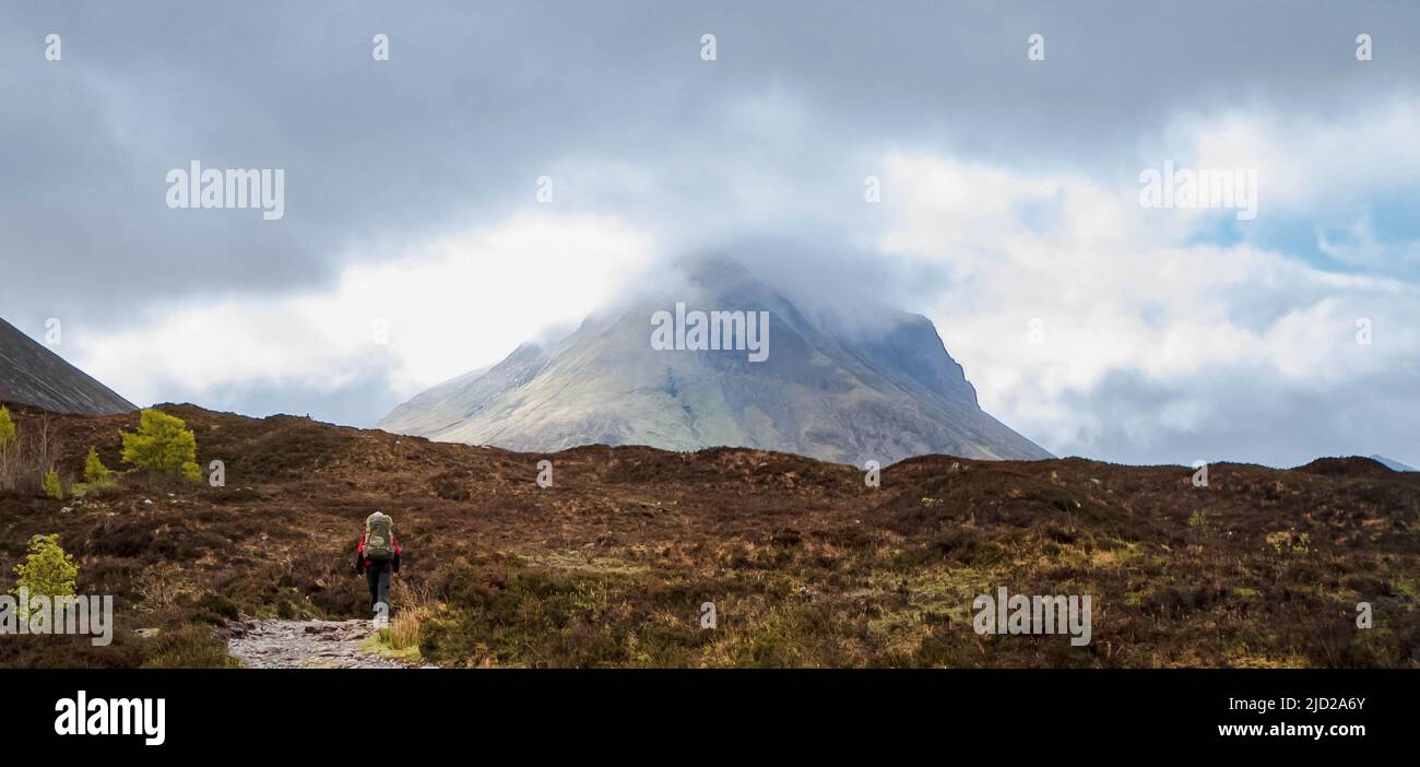 Eineinmütiger Bergsteiger, der sich in der Ferne auf der Isle of Skye, Schottland, einem riesigen Berg nähert. Stockfoto