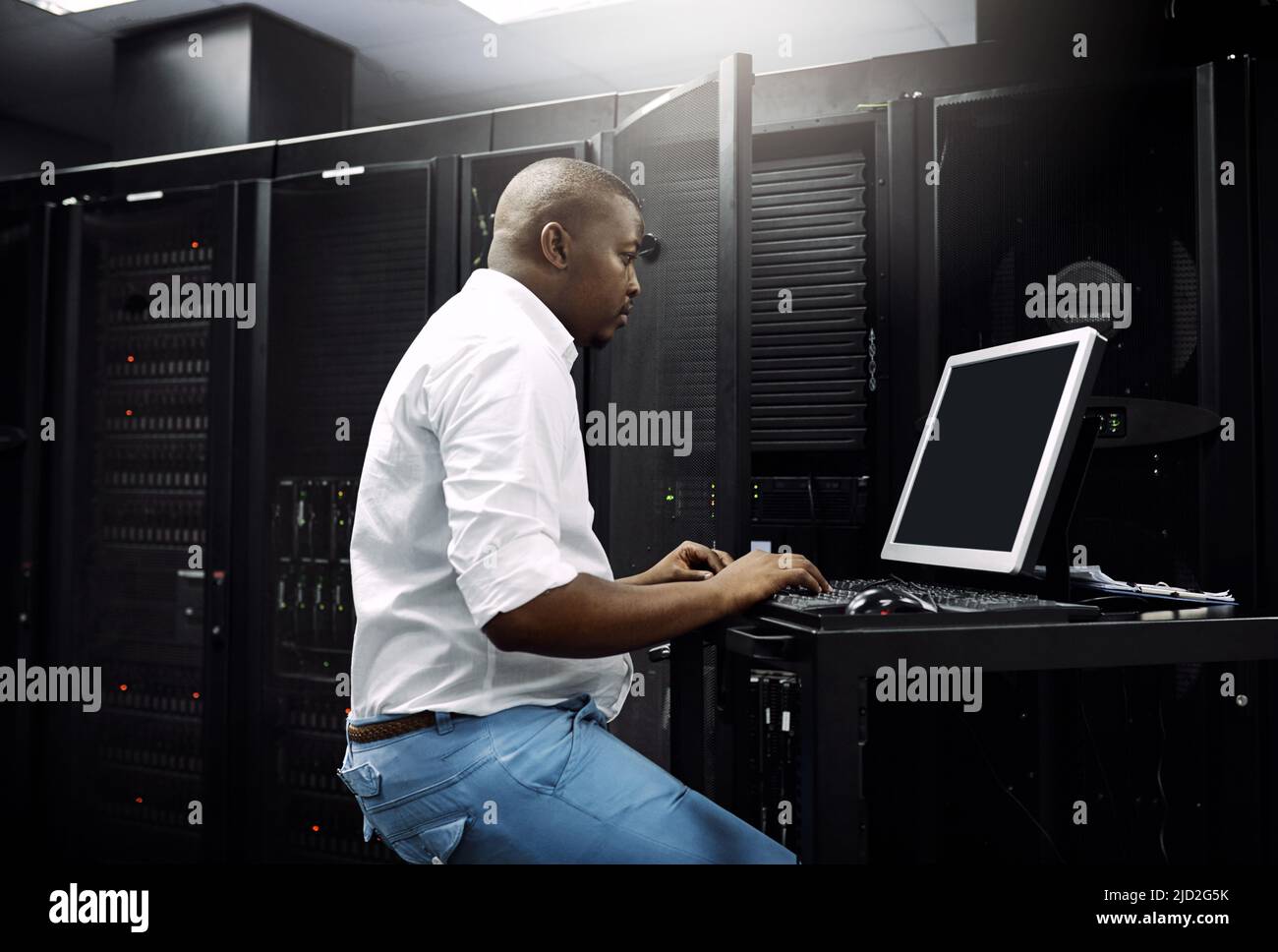 Sicherstellen, dass Ihre Server geschützt sind. Eine Aufnahme eines IT-Technikers, der einen Computer verwendet, während er im Serverraum eines Rechenzentrums arbeitet. Stockfoto