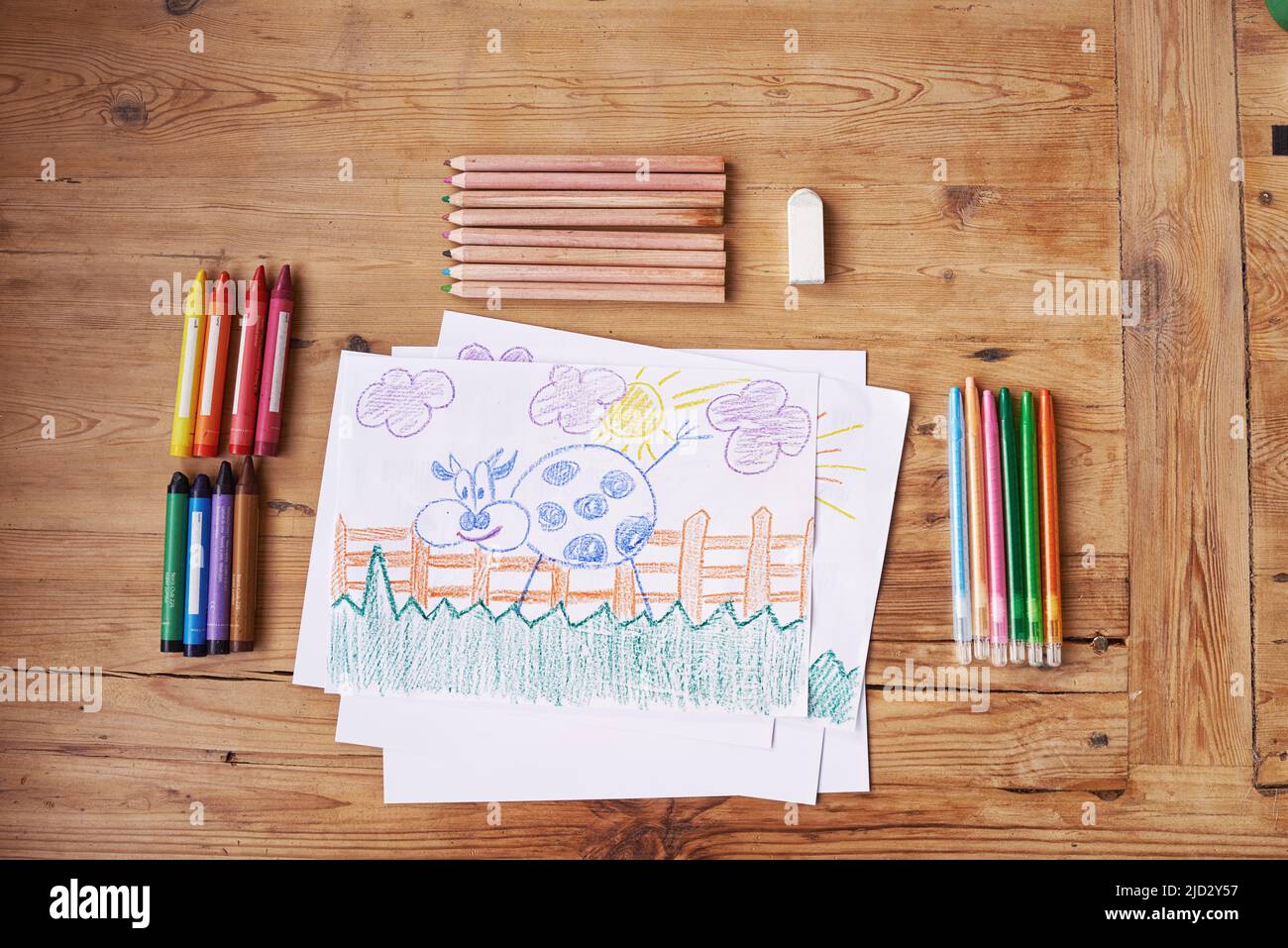 Kreativität ist Intelligenz, Spaß zu haben. Aufnahme einer Zeichnung mit Malutensilien und Bleistiften auf einem Holztisch. Stockfoto